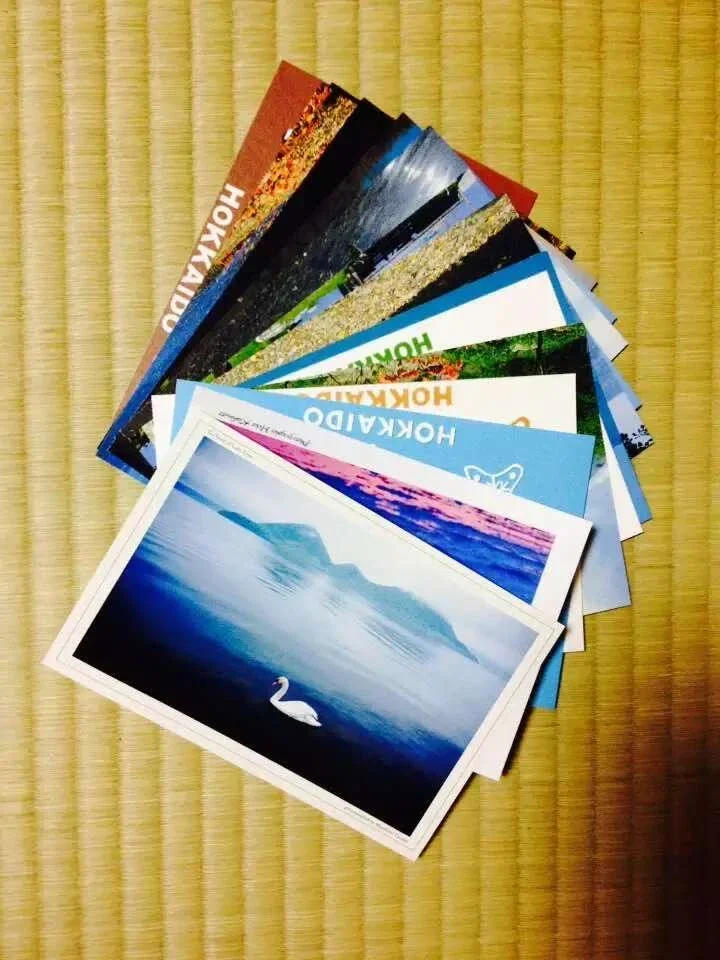 A fan of a dozen Hokkaido picture postcards on a tatami mat, a swan on a blue lake on top.